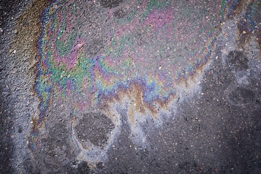Colorful gasoline or oil spill creating a rainbow pattern on asphalt, indicating pollution and environmental damage.