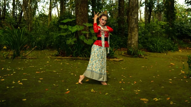 A Javanese dancer wears an elegant red costume and emphasizes the elegance of his movements when dancing in the forest in the morning