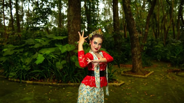 A Javanese dancer wears an elegant red costume and emphasizes the elegance of his movements when dancing in the forest in the morning
