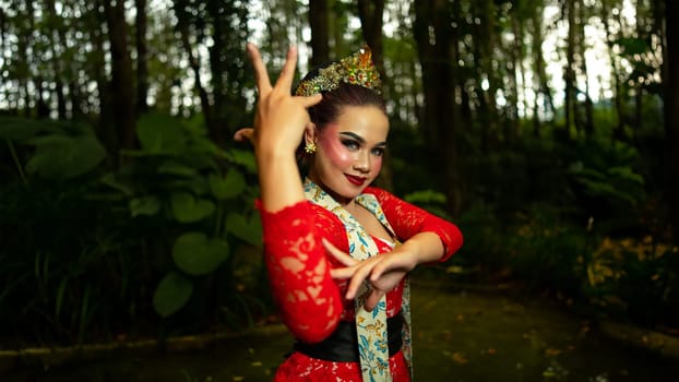 A Javanese dancer wears an elegant red costume and emphasizes the elegance of his movements when dancing in the forest in the morning