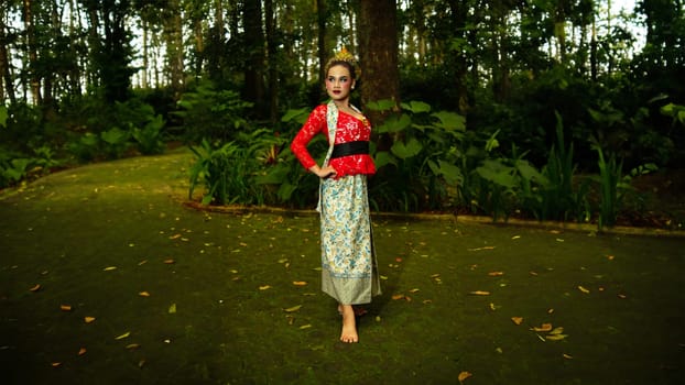 A traditional dancer called ronggeng dazzlingly stands in the forest with great elegance and striking red costume in the morning
