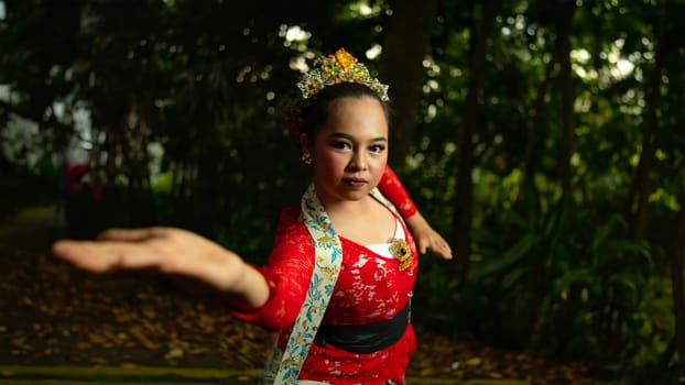 A traditional Indonesian dancer wearing a red costume decorated with sequins and embroidery looks luxurious in the dancer's performance in the forest in the morning
