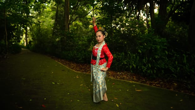 A traditional Indonesian dancer wearing a red costume decorated with sequins and embroidery looks luxurious in the dancer's performance in the forest in the morning