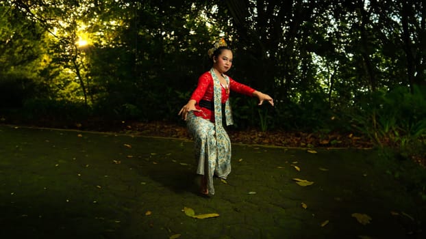 A traditional Indonesian dancer wearing a red costume decorated with sequins and embroidery looks luxurious in the dancer's performance in the forest in the morning