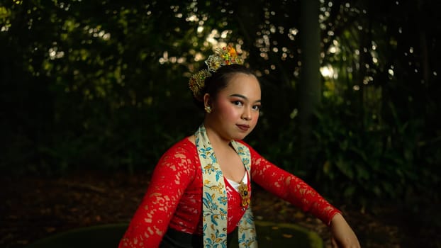 A traditional Indonesian dancer wearing a red costume decorated with sequins and embroidery looks luxurious in the dancer's performance in the forest in the morning