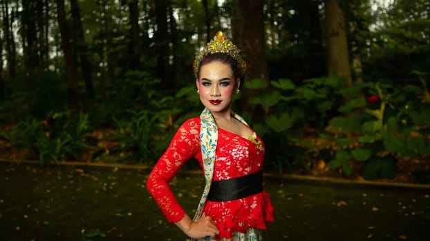 A traditional dancer called ronggeng dazzlingly stands in the forest with great elegance and striking red costume in the morning
