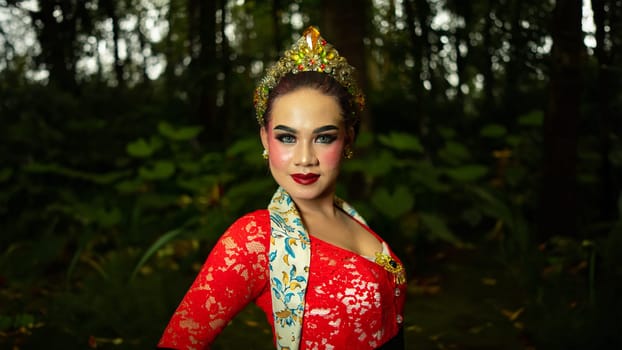 A traditional dancer called ronggeng dazzlingly stands in the forest with great elegance and striking red costume in the morning