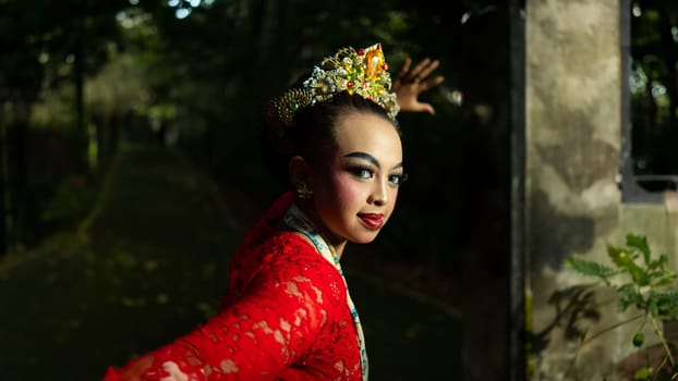 A traditional Indonesian dancer dazzles with her beautiful appearance while wearing a red costume that catches the eye of the audience in the forest in the morning