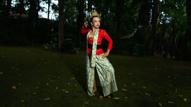 A traditional Indonesian dancer dazzles with her beautiful appearance while wearing a red costume that catches the eye of the audience in the forest in the morning
