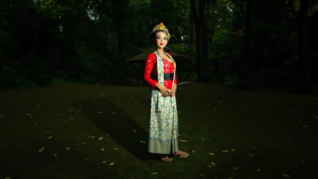 A traditional Indonesian dancer dazzles with her beautiful appearance while wearing a red costume that catches the eye of the audience in the forest in the morning