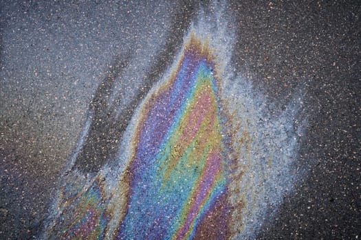 Gasoline or oil spill creating rainbow colors on asphalt road surface.
