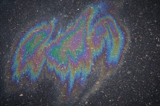 Gasoline or oil spill on asphalt creating rainbow sheen reflecting light.