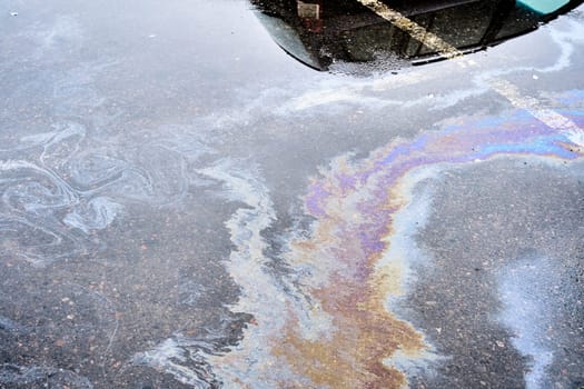 The wet asphalt in a parking lot near a hypermarket is stained with gasoline and oil spill