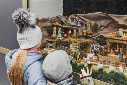Children are looking at a Christmas nativity scene with baby Jesus Creche Figurines in a shop window