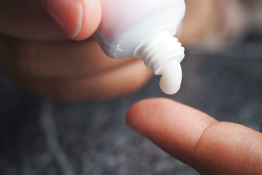 A finger dipped in cream from a tube, perfectly poised and ready for application on skin