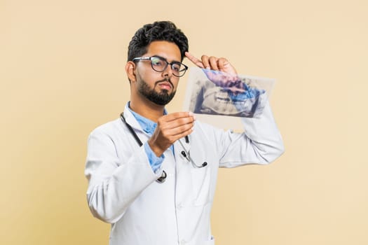 Indian young doctor orthodontist man examines a panoramic x-ray picture of the jaw teeth. 3D model of the patient's mouth, MRI scan. Dentistry, oral care. Arabian stomatology guy on beige background