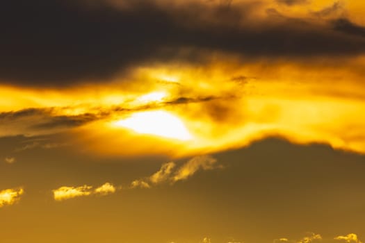 Beautiful cloudy yellow sunset with gigantic sun over big fields and trees seen by 600mm camera lens 