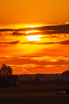 Beautiful cloudy red sunset with gigantic sun over big fields and trees seen by 600mm camera lens 