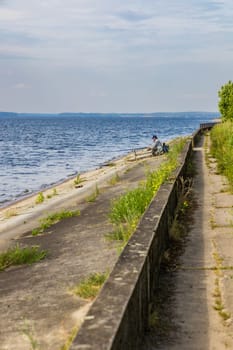 Old fisherman in hat and dark glasses do fishing at the coast of big lake at sunny morning