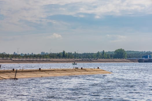 Small bay behind small local harbor at the coast of big lake next to water dame and road