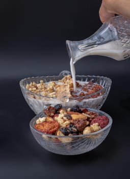 Pouring milk into the Cereal in Glass bowl served with Tasty Gadola in dark background. Healthy breakfast concept, Space for text, Selective focus.