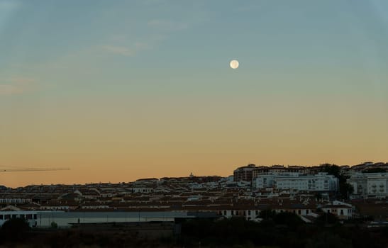 sunrise cityscape with reddish and blue tones with a full moon in the sky