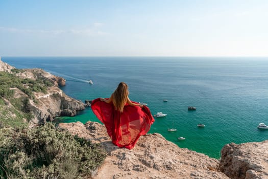 Woman sea red dress yachts. A beautiful woman in a red dress poses on a cliff overlooking the sea on a sunny day. Boats and yachts dot the background