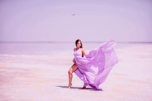 Woman pink salt lake. Against the backdrop of a pink salt lake, a woman in a long pink dress takes a leisurely stroll along the white, salty shore, capturing a wanderlust moment