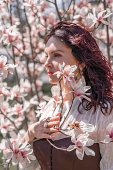 Magnolia park woman. Stylish woman in a hat stands near the magnolia bush in the park. Dressed in white corset pants and posing for the camera