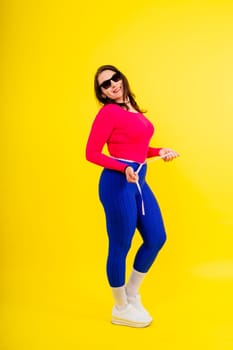 Overweight woman measuring waist before weight loss in a studio shot on yellow background