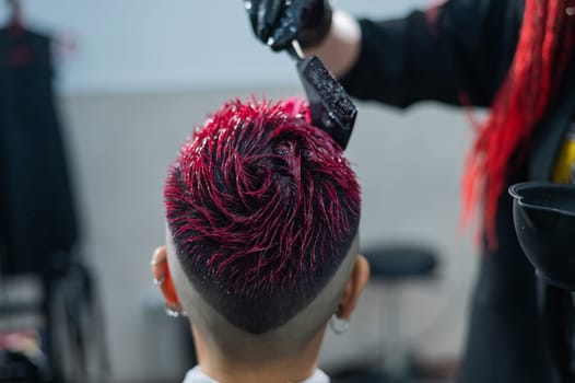Close-up of the process. The hairdresser dyes the hair of an Asian woman in pink. Short extreme haircut