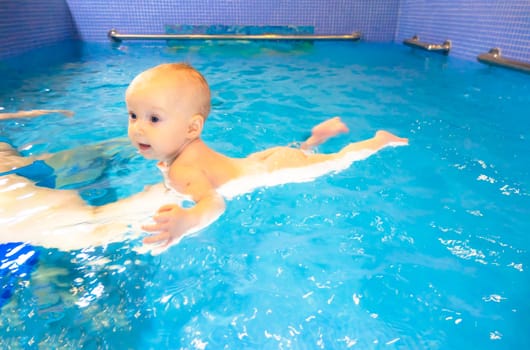 Adorable baby girl enjoying swimming in a pool with her mother early development class for infants teaching children to swim and dive. Swimming instructor doing exercises with a small child in the pool . High quality photo