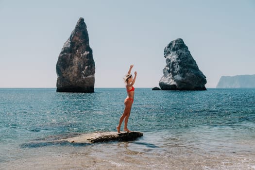 Woman travel sea. Young Happy woman in a long red dress posing on a beach near the sea on background of volcanic rocks, like in Iceland, sharing travel adventure journey