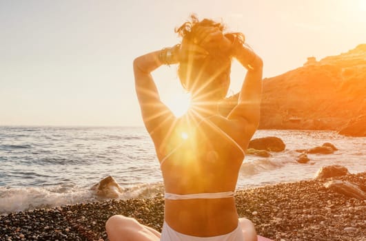 Young woman in swimsuit with long hair practicing stretching outdoors on yoga mat by the sea on a sunny day. Women's yoga fitness pilates routine. Healthy lifestyle, harmony and meditation concept.