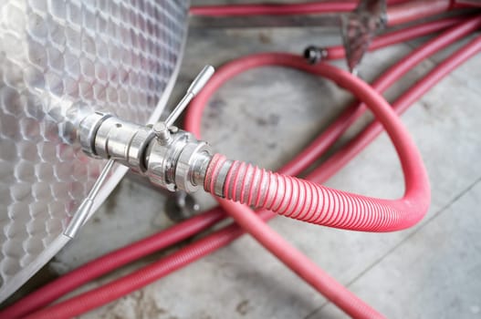 Red faucet connected to steel barrel in factory closeup. Chemical industry concept