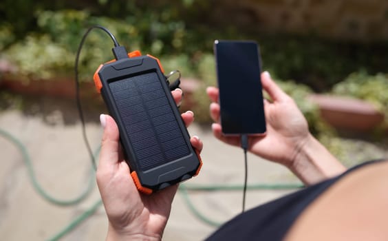 Female hand holding solar power bank and mobile phone closeup. Modern energy-saving devices concept