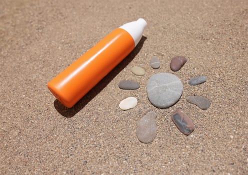 Sun made of stones on sea sand orange liquid bottle of cream or lotion. Sun protection and sunscreen lotion or spray spf