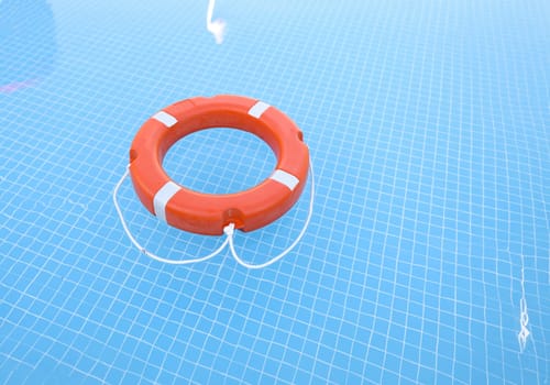 Lifebuoy on blue water with sun glare. Water safety concept