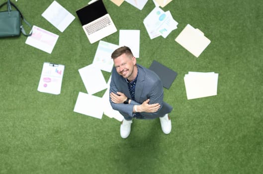 Businessman looks up on green lawn with laptop and financial business chart. Successful self-confident man and successful career