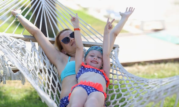 Loving family mom and daughter spend time together in summer hammock. Family happy joyful vacation in summer garden