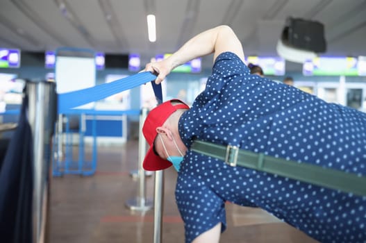 Man in a protective mask raises access tape and goes to registration without queue. Violation of rules of medical and passport control in public places airport station