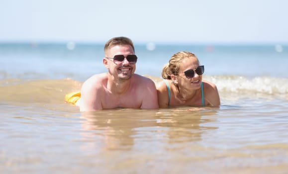 Happy couple in sunglasses lies on beach in sea. Sea summer vacation emotions and romantic trips