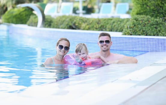 Portrait of young family with smiling child in pool. Happy joyful family together in pool