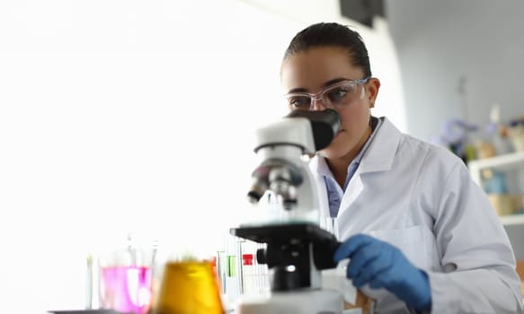 Young woman scientist looks into microscope. Doctor using microscope in laboratory examines tests