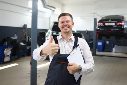 Happy smiling auto mechanic showing thumbs up gesture in workshop. Quality car service recommendation