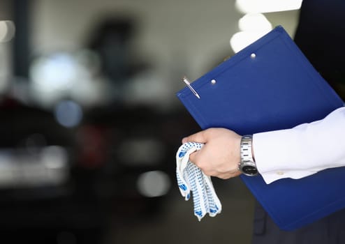 Car mechanic priemchik holds gloves and clipboard in car service. Car insurance and maintenance after a breakdown or accident