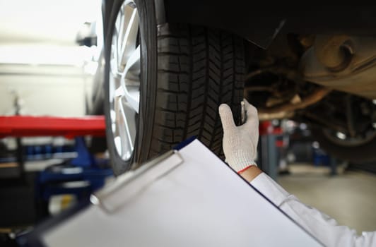 Man mechanic working under car at car service station. Experienced mechanic examines car tires