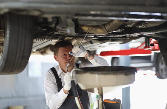 Auto mechanic checks running gear of car and oil leak at service station. Male worker fixing breakdown problem with a machine