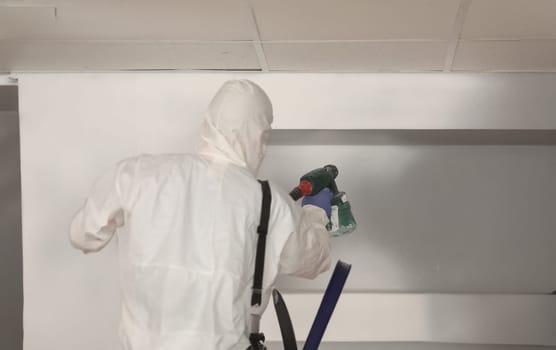 Worker paints wall white with spray gun. Painter in protective suit with spray gun concept