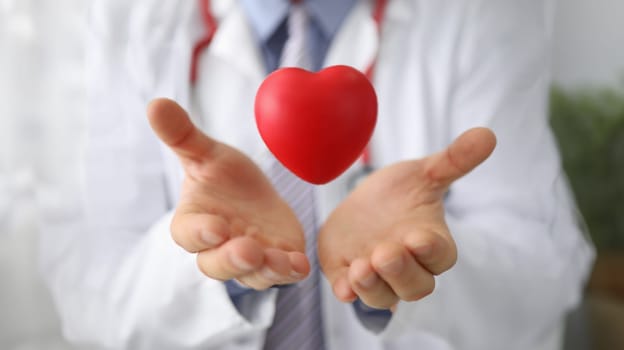 Doctor cardiologist holds hands and airborne red toy heart closeup. Cardiotherapist and treatment of heart diseases